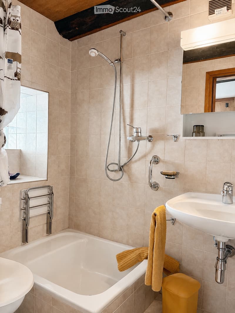 Bathroom with beige tiled walls, a bathtub, a sink, a showerhead, a mirror, and a towel hanging on a rack.