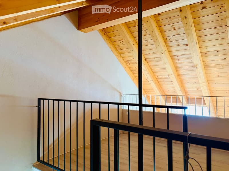 Staircase with wooden ceiling beams, metal railing, and light-colored wooden flooring.