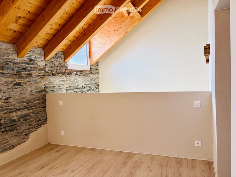 Empty room with wooden flooring, exposed wooden beams on the ceiling, and a stone accent wall. A small window is visible in the stone wall.