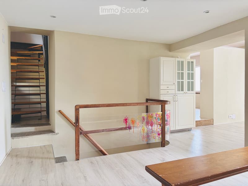 Bright hallway with wooden flooring, staircase leading upwards, white cabinet, and a colorful glass panel on the railing.