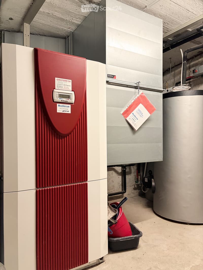 Utility room with a red water heater, grey boiler, and a red bucket on the floor.