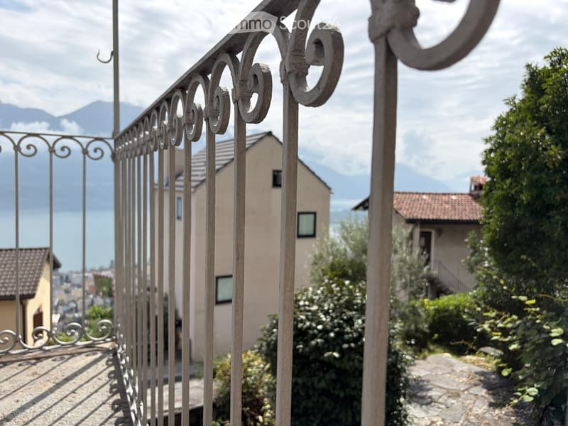 Balcony with ornate metal railing, overlooking a scenic view of houses, greenery, and distant mountains.