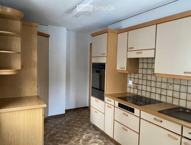 Modern kitchen with light wood cabinets, stainless steel appliances, and a tiled backsplash.
