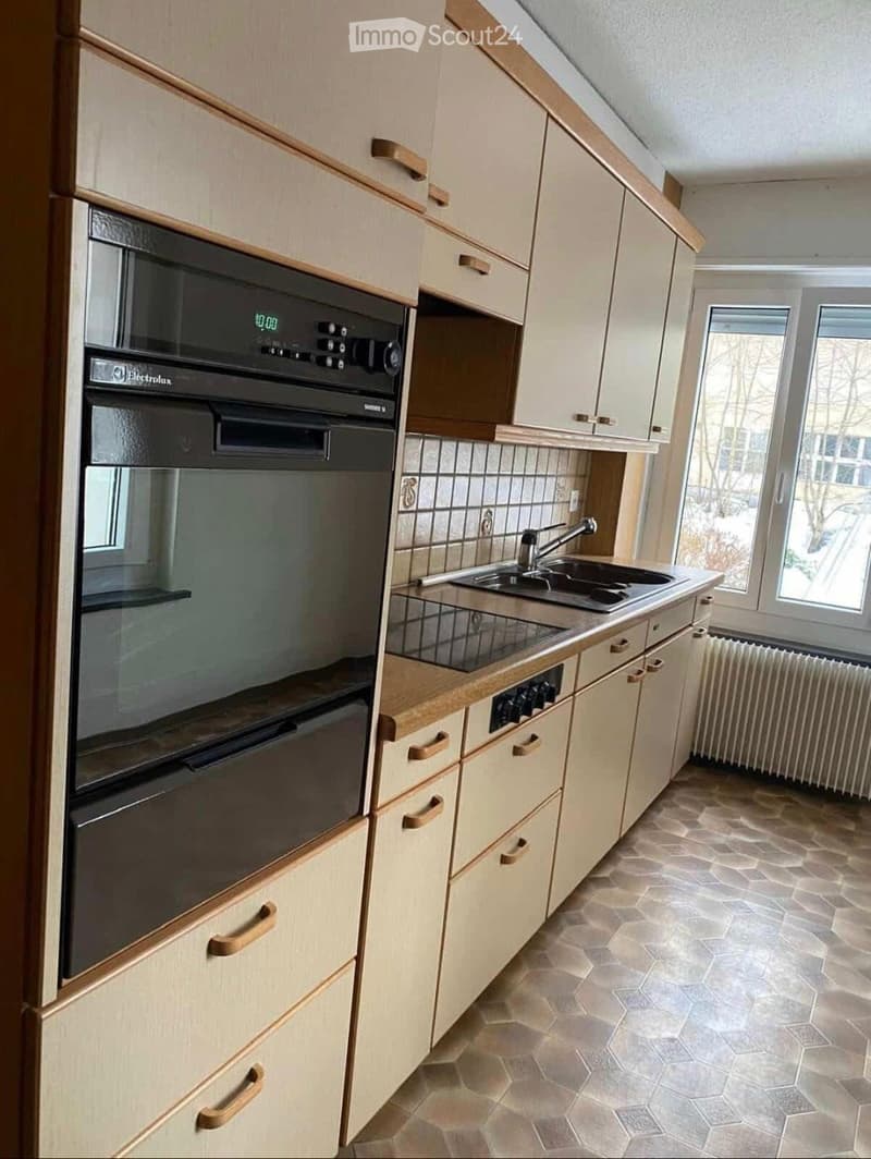 Modern kitchen with light-colored cabinets, a stainless steel oven, a sink with a faucet, and tiled flooring.