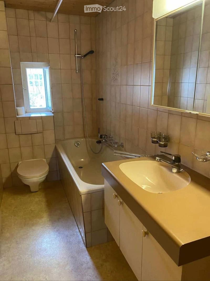 Bathroom with a toilet, bathtub, sink, and mirror. The room features tiled walls and a small window providing natural light.