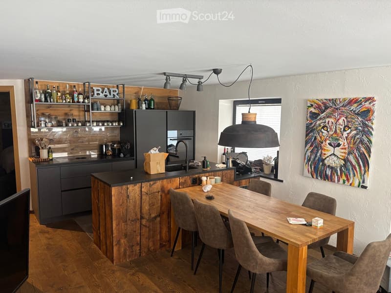 Modern kitchen with wooden island, dining table, bar area, and colorful lion painting on wall.