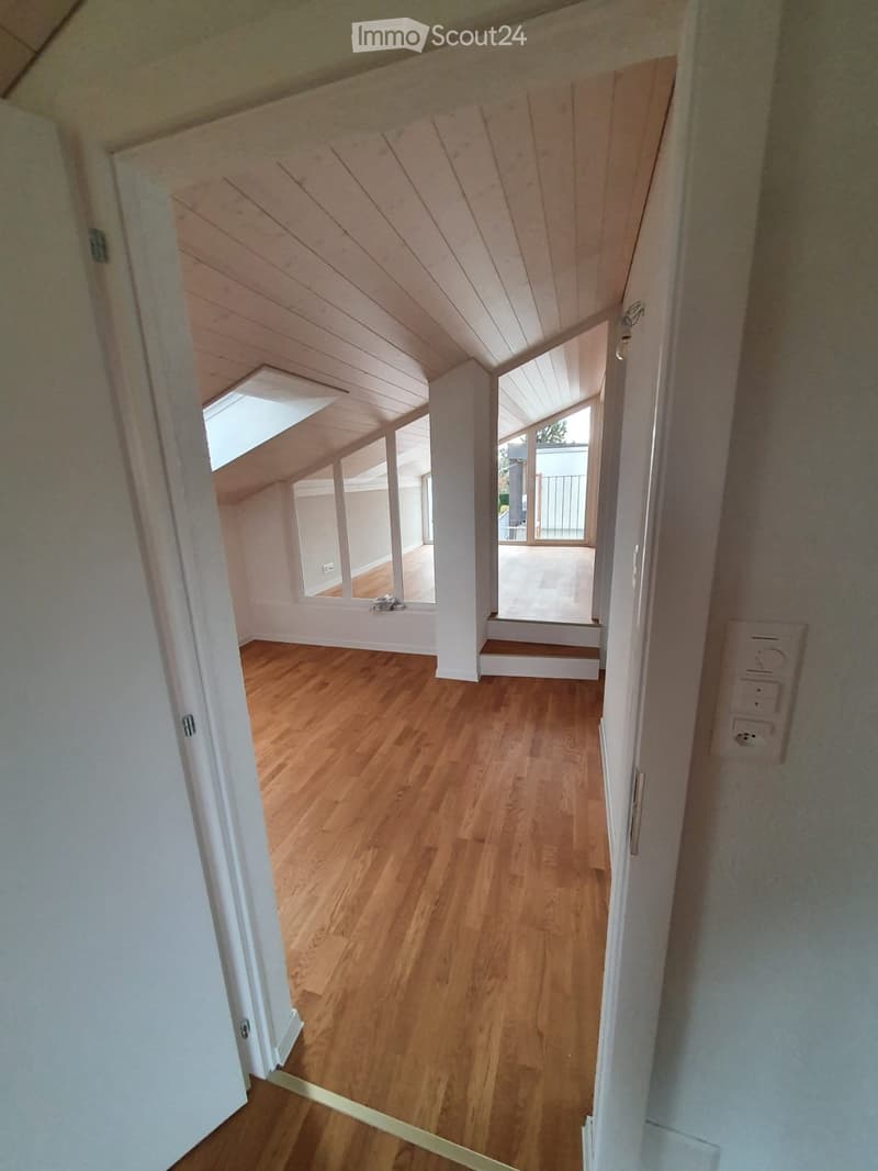 Empty hallway with wooden flooring, white walls, and multiple doors leading to rooms with large windows and skylights.