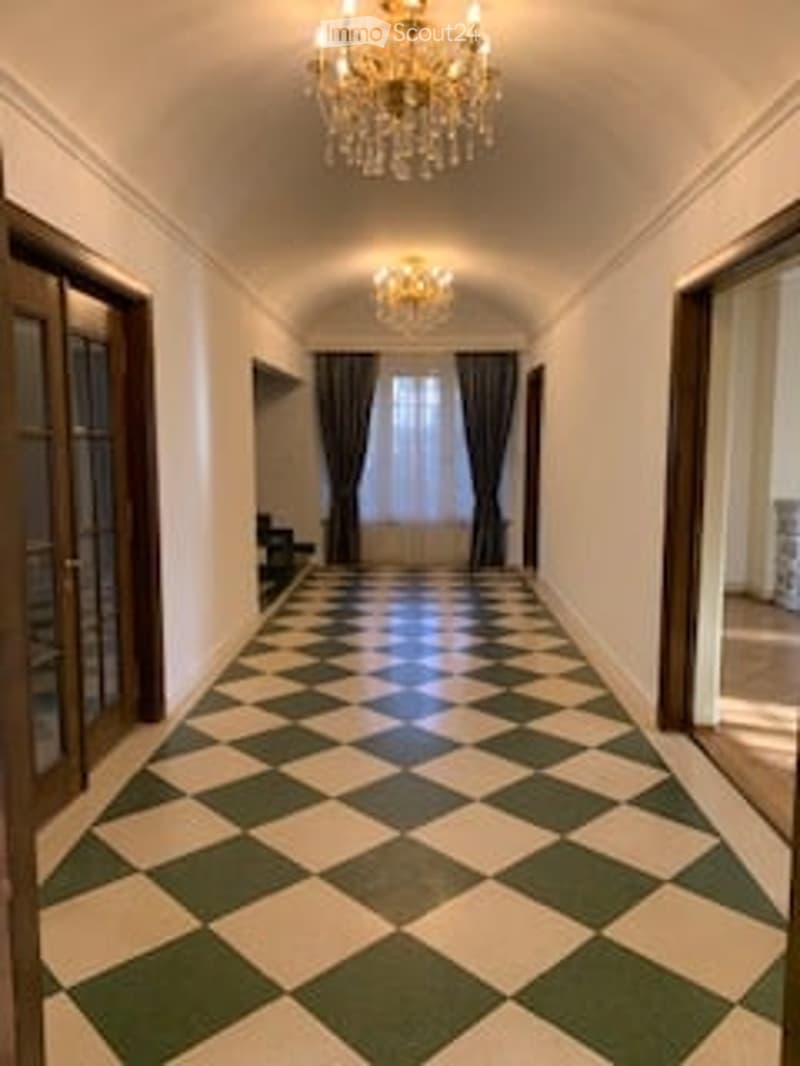 Elegant hallway with checkered black and white floor, large wooden doors, and ornate chandeliers.