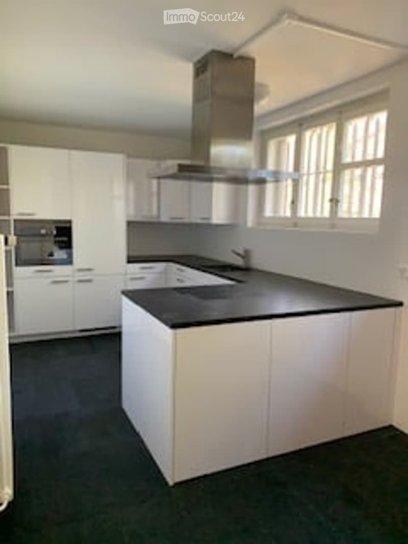 Modern kitchen with white cabinets, black countertop, island, sink, oven, and range hood.
