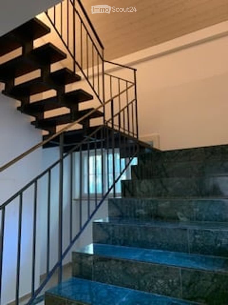 Staircase with dark wooden steps and a metal railing, leading up to a higher level. The walls are painted a light color, and the floor has a polished finish.
