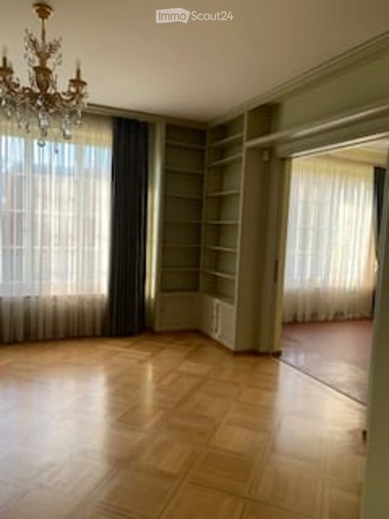 Empty room with wooden flooring, large windows with curtains, built-in shelving, and a chandelier.