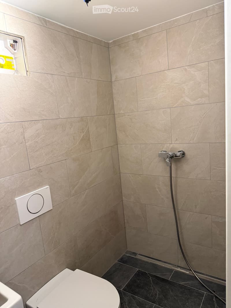 Modern bathroom with beige marble tiles, a toilet, and a handheld showerhead with a control panel.