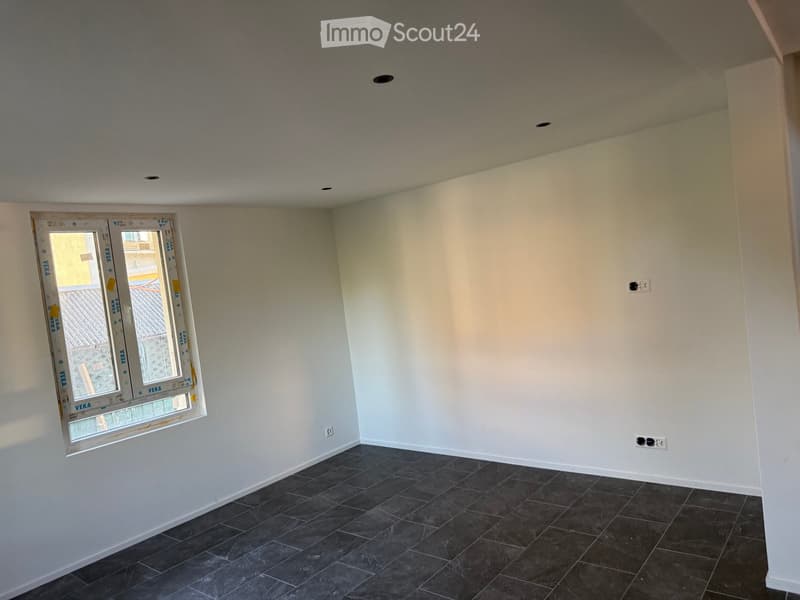Empty room with dark tiled floor, white walls, and a window with protective film. No furniture or equipment present.