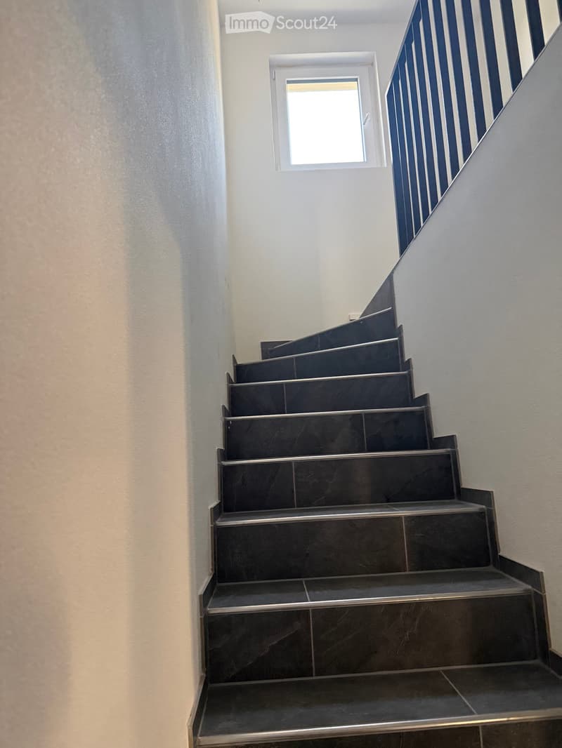 Modern staircase with dark marble steps and metal railings, illuminated by a small window at the top.