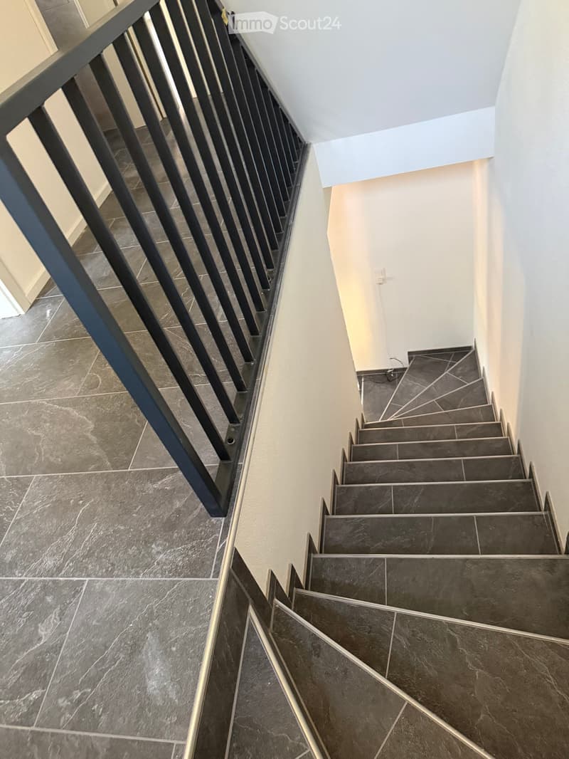 Modern staircase with dark tiled steps and a sleek black metal railing, leading upwards with a clean, contemporary design.