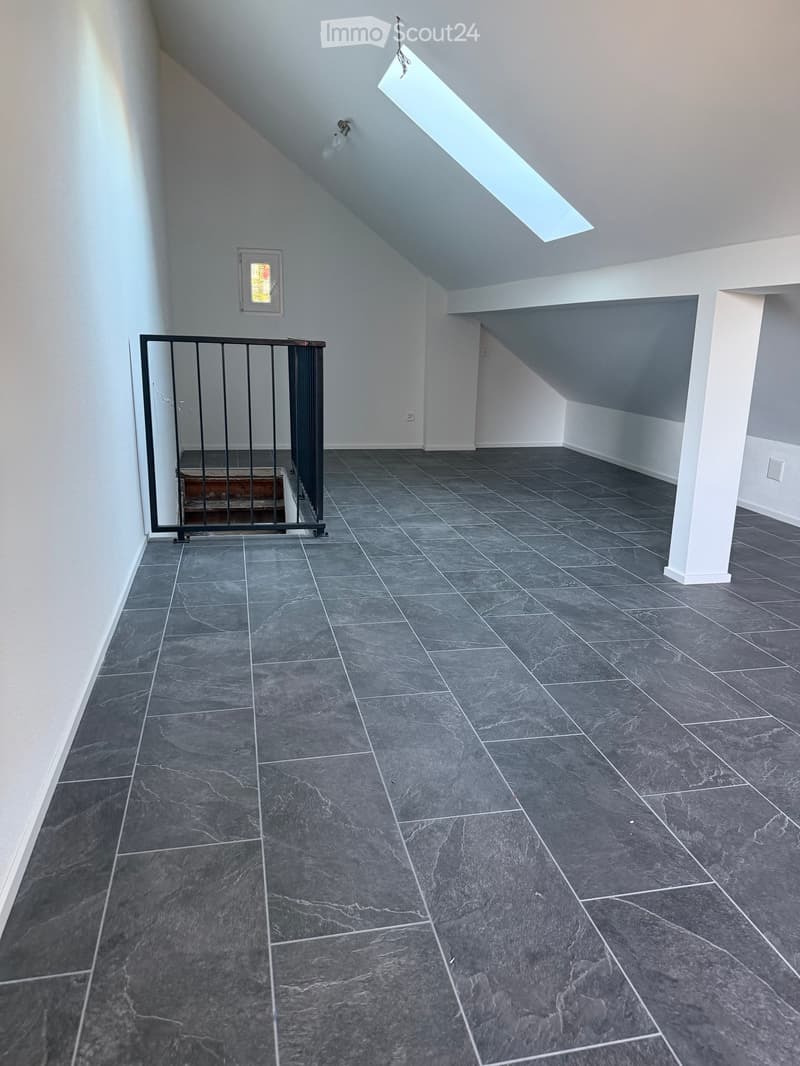 Empty room with grey tiled floor, white walls, and a small window. A black safety gate is visible on the left side.