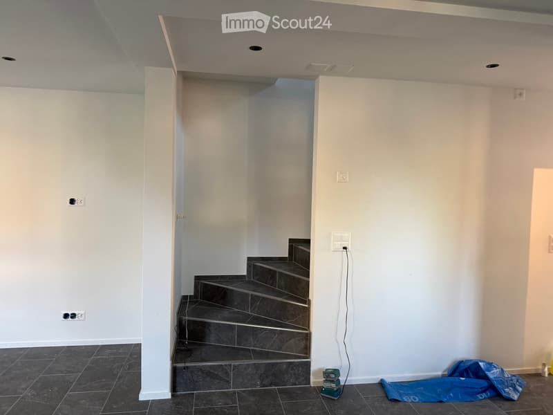 Empty room with white walls, dark tiled floor, and a staircase leading upwards. No furniture or equipment visible.