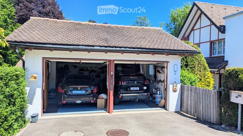 Two-car garage with two luxury cars inside, attached to a two-story house with a tiled roof and white exterior.