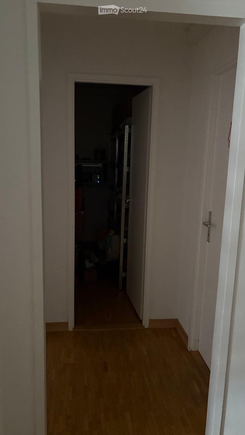 Empty hallway with wooden flooring and white walls, leading to a partially visible room with furniture.