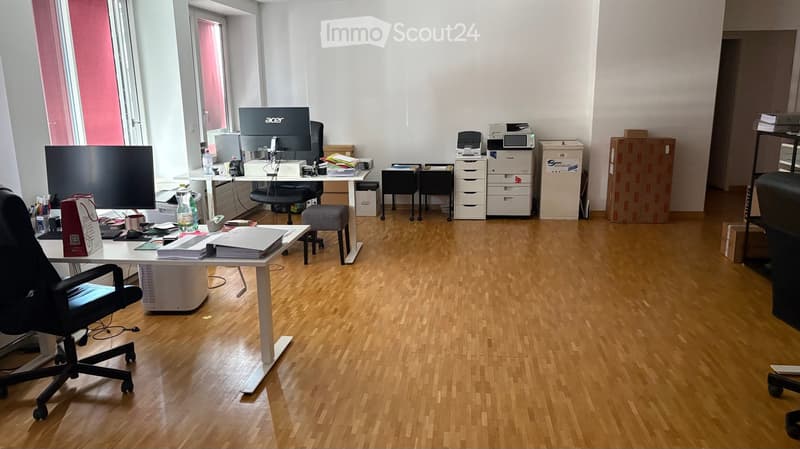 Office space with wooden flooring, desks, chairs, computer screens, printers, and a stool.