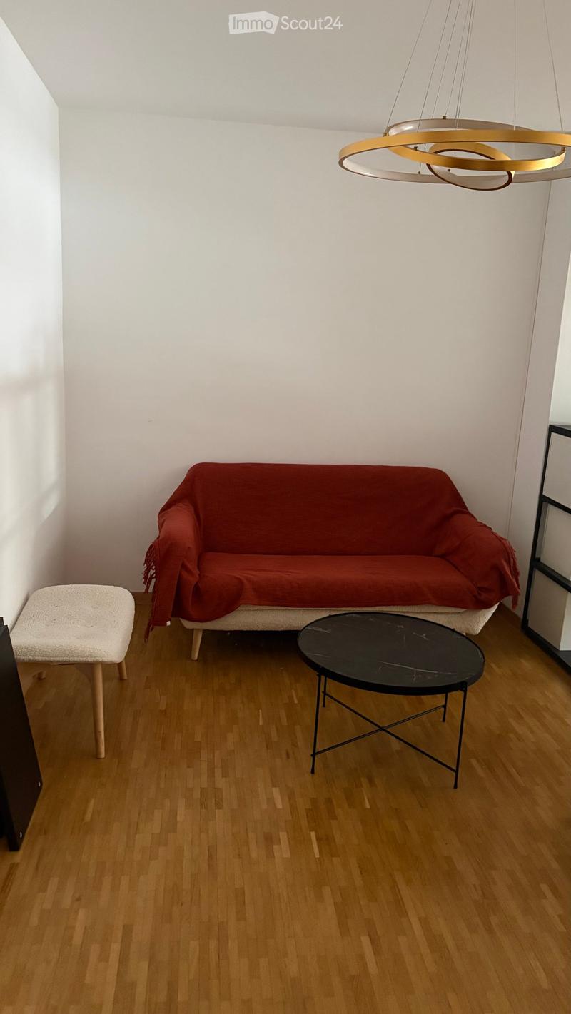 Living room with wooden flooring, a red sofa, a black coffee table, and a white stool.