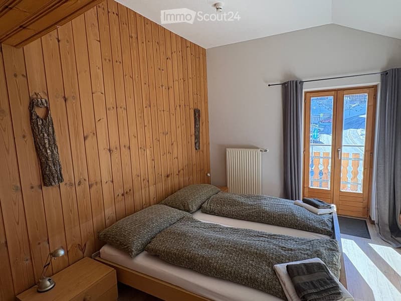 bedroom with wooden walls, two single beds, wooden nightstand, lamp, radiator, double doors leading to a balcony
