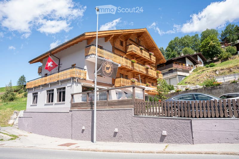 wooden chalet style house, multiple balconies, flag, cars parked in front