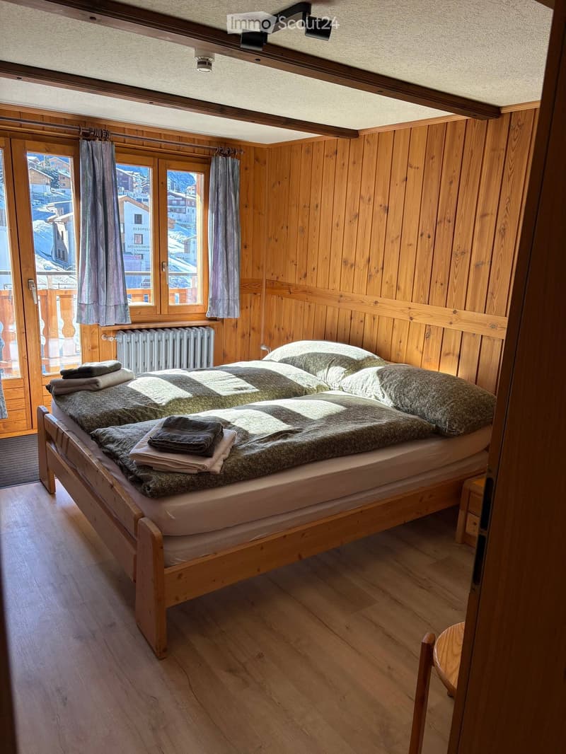 bedroom with wooden walls, wooden bed, two single beds, pillows, blankets, towels, wooden chair, wooden floor, large windows, balcony, view of the mountains