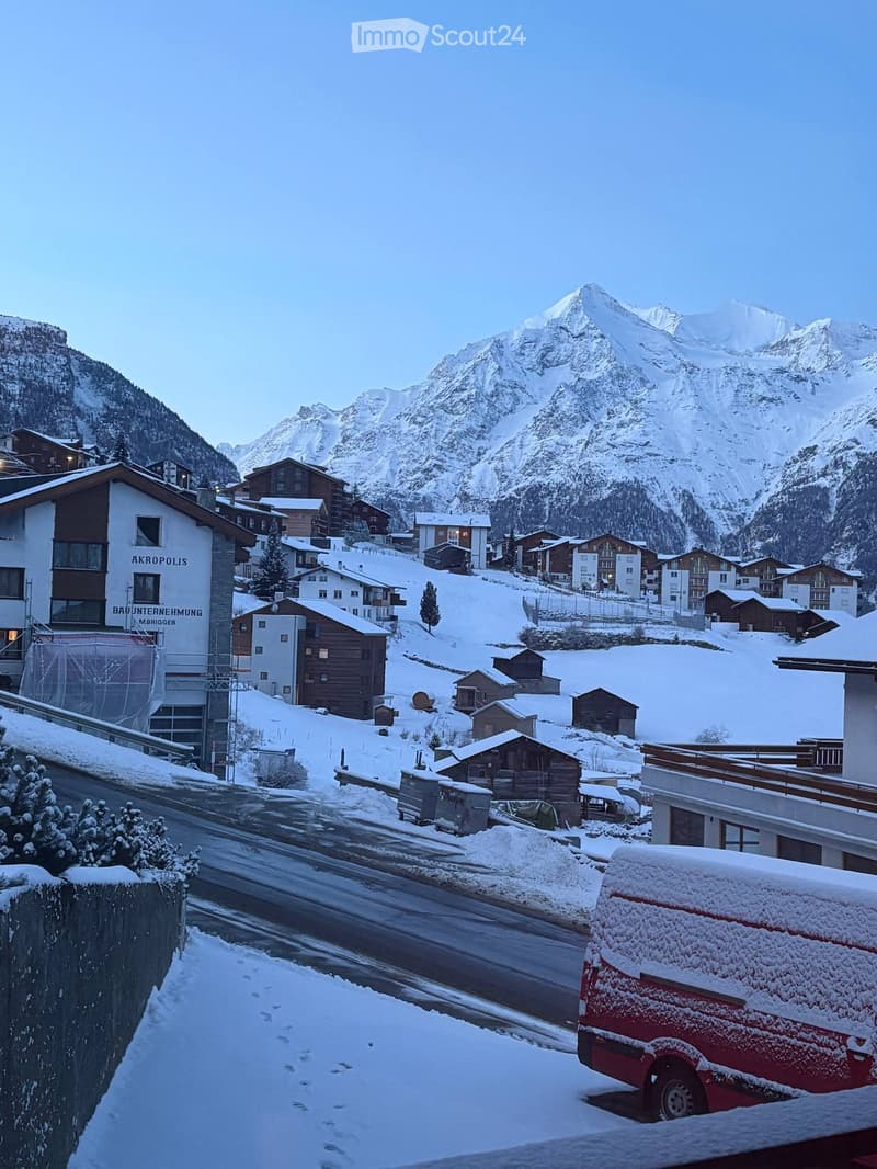 Snowy mountain village, several buildings, road, van, mountains in the background