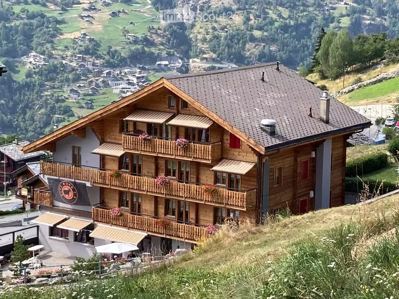 A large wooden chalet with multiple balconies and a panoramic mountain view.