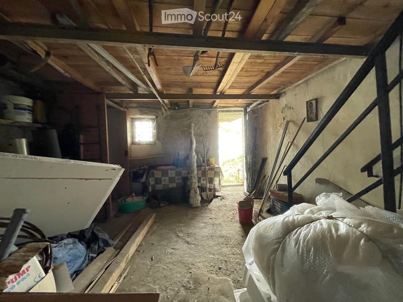 Unfurnished attic space with exposed wooden beams, concrete floor, and scattered items including tools, buckets, and a staircase leading upwards.