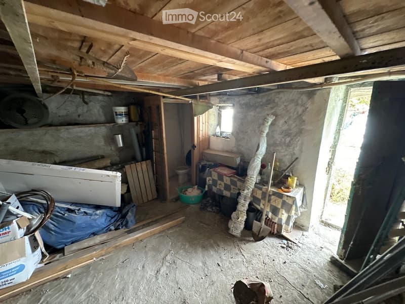 Empty unfinished basement with exposed wooden beams, concrete walls, and scattered tools and materials.
