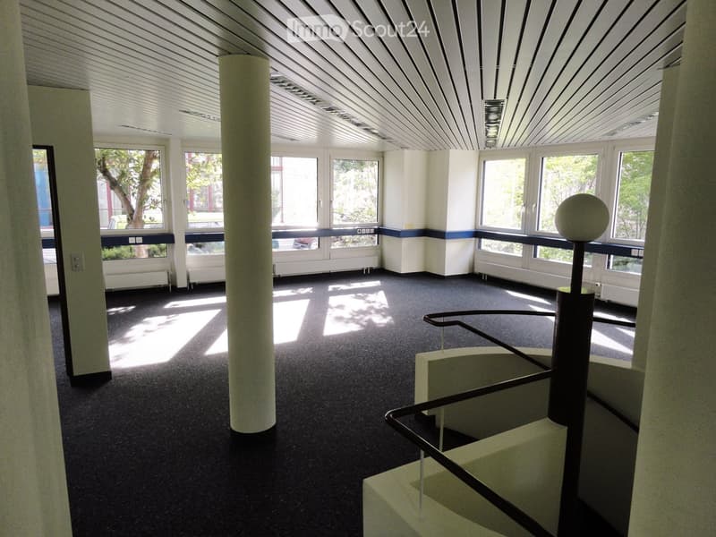 Empty room with central pillar, large windows, stair in the corner, radiators