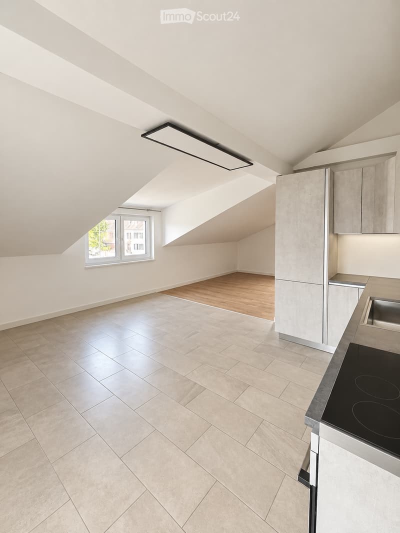 Modern kitchen with light-colored cabinets, stainless steel appliances, and a combination of tiled and wooden flooring.