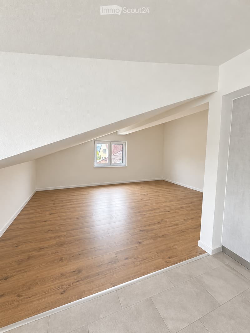 Empty room with wooden flooring and white walls, featuring a window with a view of a house and a tree outside.