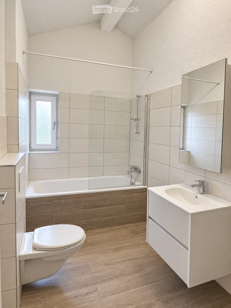 Modern bathroom with wooden flooring, white tiled walls, bathtub, toilet, sink, and a glass-enclosed shower stall.