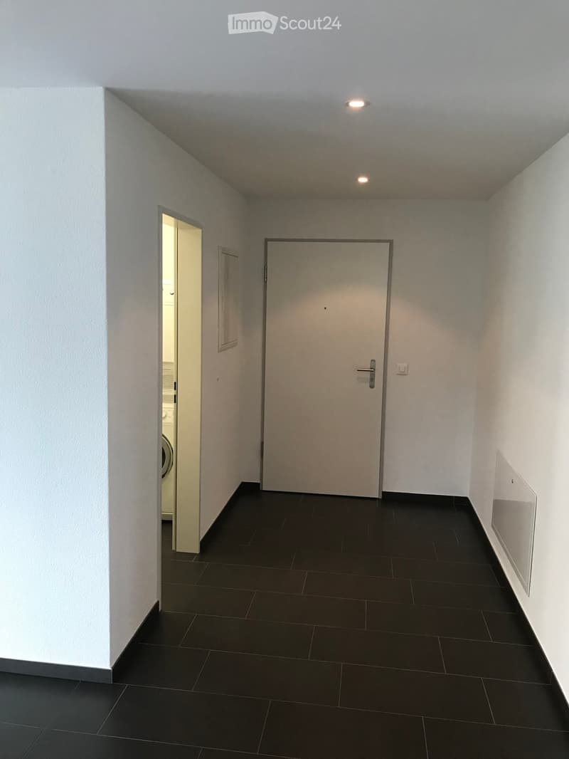Empty hallway with dark tiled floor, white walls, and two doors, one leading to a room with a washing machine visible.