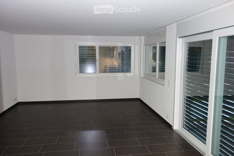 Completely empty room with bare white walls and black tiled floor. Windows with blinds are visible, but no furniture or equipment is present.