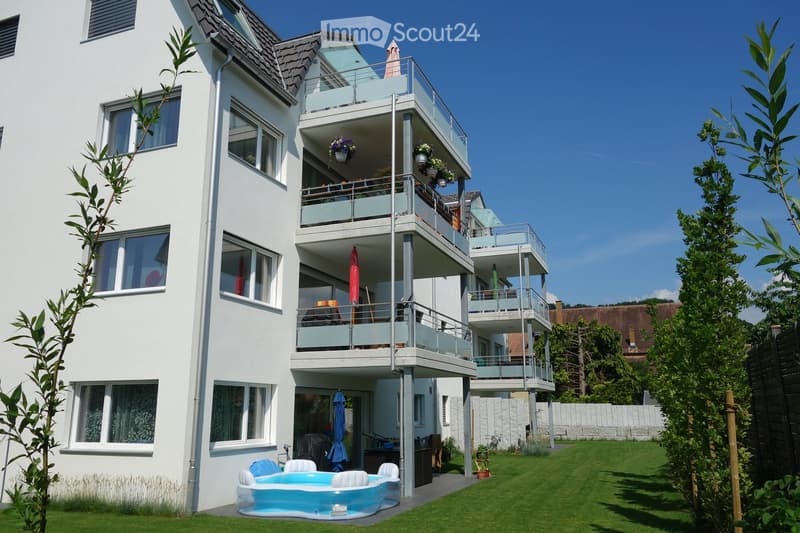 Modern three-story building with white exterior, multiple balconies, and a small swimming pool in the front yard.