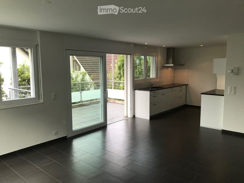 Modern kitchen with dark tiled floor, white cabinets, stainless steel sink, and range hood. Large windows and sliding glass doors lead to a balcony.