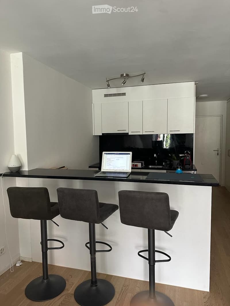 Modern kitchen with white cabinets, black countertop, three black stools, and a laptop on the counter.