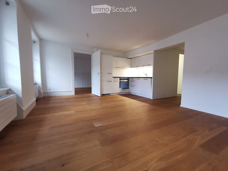Empty room with wooden floors, white walls, and white kitchen cabinets.