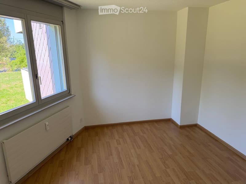 Empty room with wooden flooring, white walls, and a large window with a radiator below it.