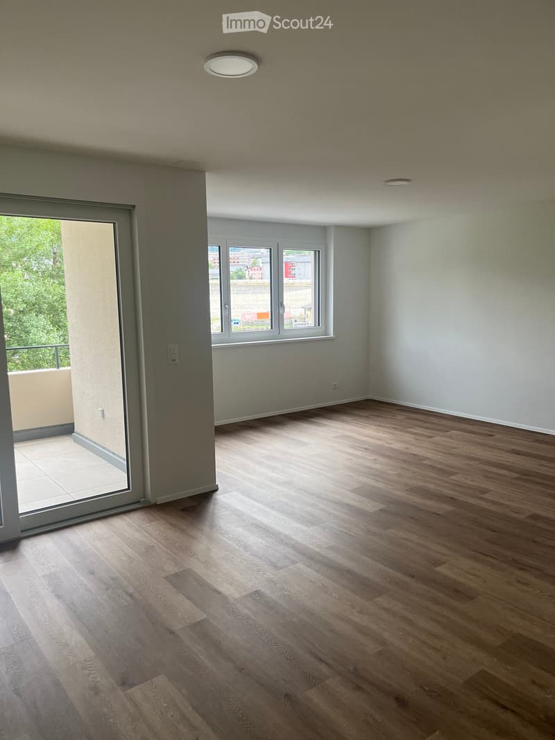 Empty room with wooden flooring, large windows, and a sliding glass door leading to a balcony.