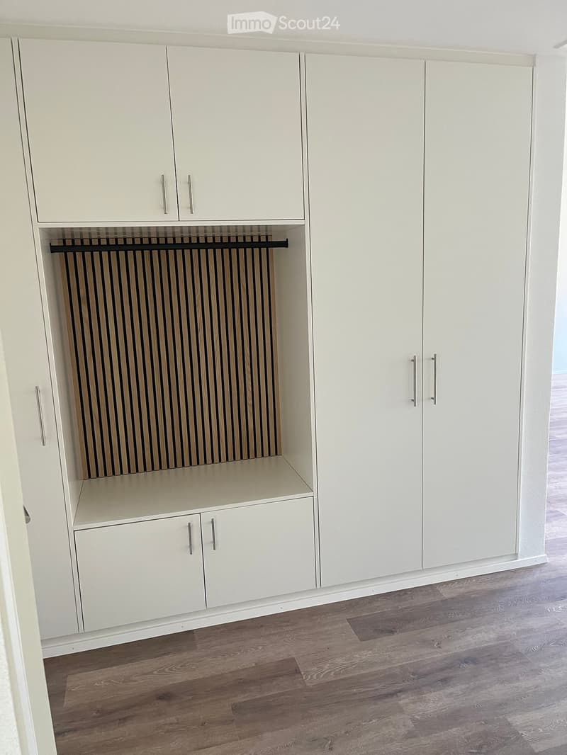 Empty room with white built-in wardrobes and a radiator, featuring a wooden floor.