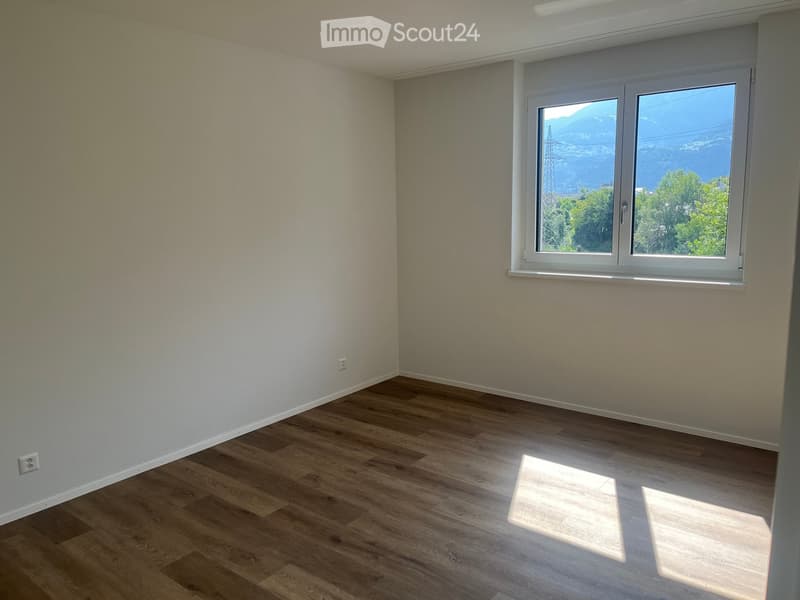 Empty room with wooden flooring and white walls, featuring a large window with a scenic mountain view.