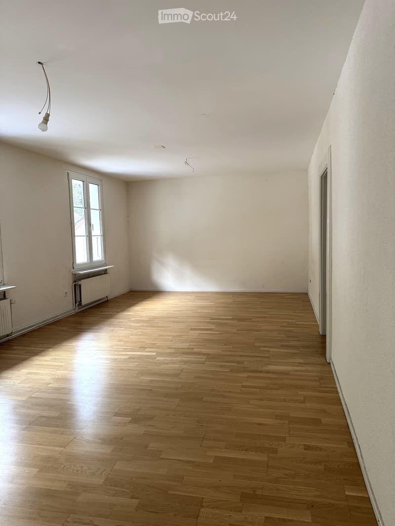 Empty room with wooden flooring, white walls, and a single window with a radiator below it. The room has a simple, clean design with no furniture or decorations.