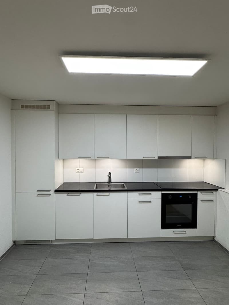 Modern kitchen with white cabinets, stainless steel sink, and built-in oven. Grey tiled floor and walls.