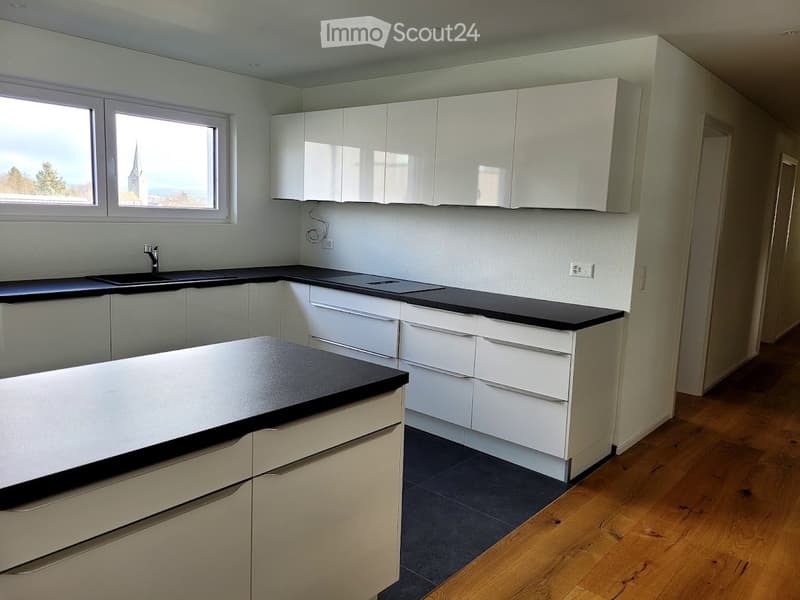 Empty kitchen with white cabinets, black countertops, and wooden flooring. No appliances or furniture present.