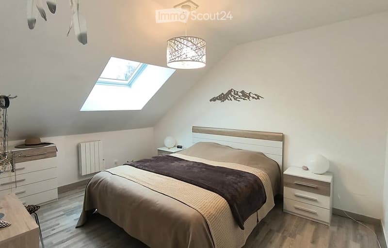 Cozy attic bedroom with wooden flooring, skylight window, modern bed with brown bedding, nightstands with lamps, and a decorative mountain wall art.